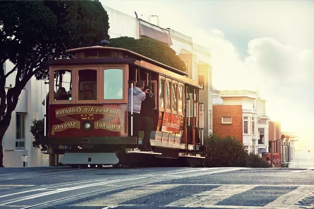 Eine Seilbahn fährt um einen Hügel in San Francisco, während die Passagiere aus dem Fenster schauen.